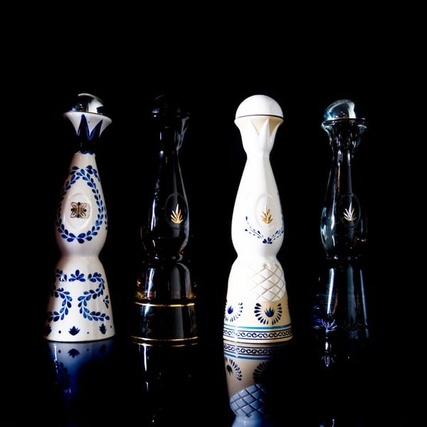 Four decorative tequila bottles, two white with blue patterns and two dark, on a reflective black surface.