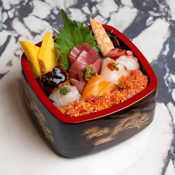 A colorful chirashi bowl with various sashimi, tamago, and shrimp, served in a decorative black and red bowl.