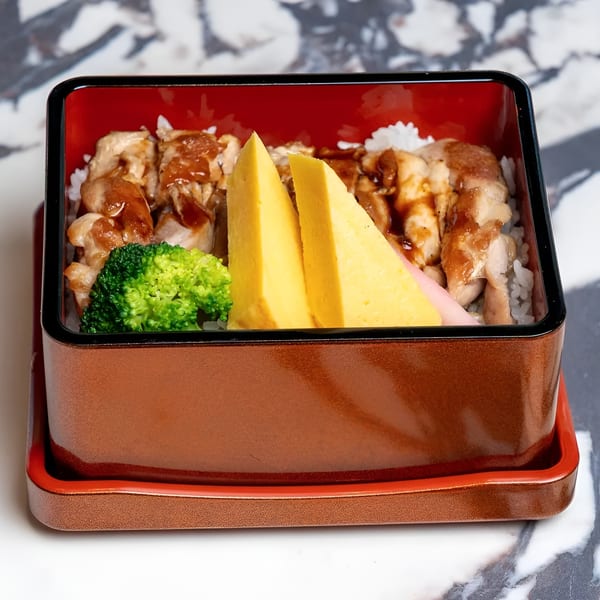 A bento box filled with teriyaki chicken, white rice, broccoli, and two pieces of tamagoyaki.