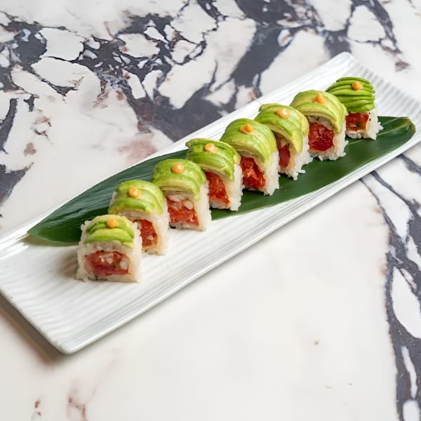 Eight pieces of sushi with red tuna and avocado slices on a white rectangular plate.