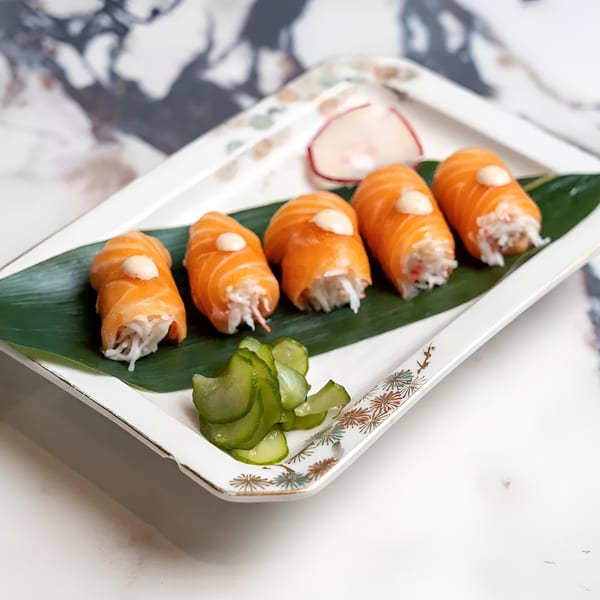 Five salmon-wrapped sushi rolls with crab, topped with sauce, served on a leaf with pickles and radish.