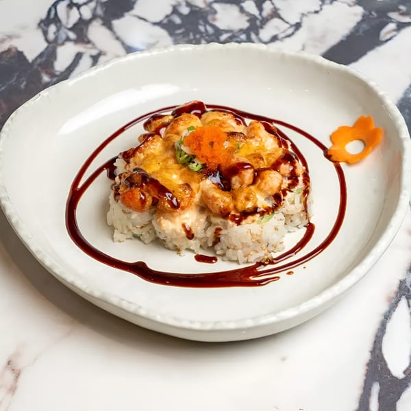 Baked sushi with melted cheese, orange roe, green onions, and a dark sauce swirl on a white plate.
